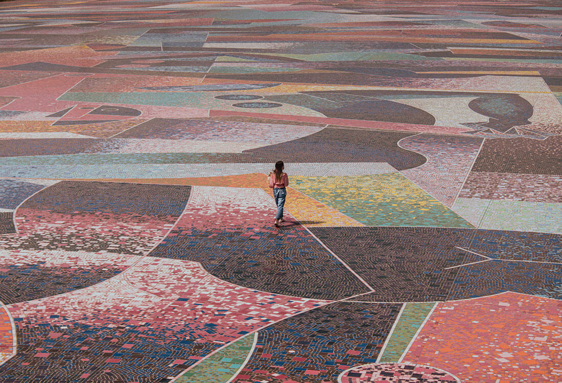 Photo of a lady walking across a large area paved in colorful mosaic tile